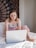 A confident young woman smiling while browsing an online store on her laptop.
