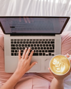 person using MacBook Pro and holding cappuccino