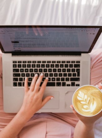 person using MacBook Pro and holding cappuccino