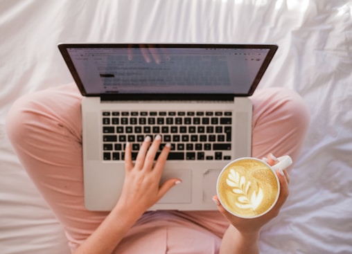 person using MacBook Pro and holding cappuccino