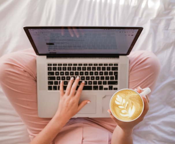 person using MacBook Pro and holding cappuccino