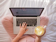 person using MacBook Pro and holding cappuccino
