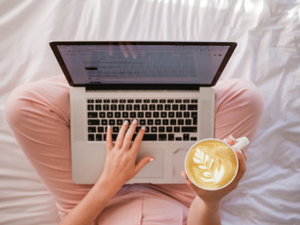 person using MacBook Pro and holding cappuccino