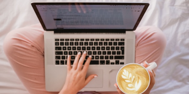 person using MacBook Pro and holding cappuccino
