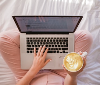 person using MacBook Pro and holding cappuccino