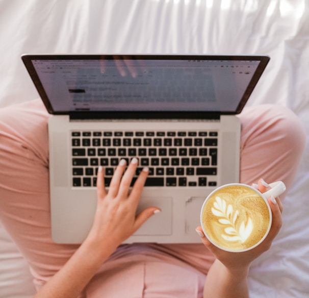 person using MacBook Pro and holding cappuccino