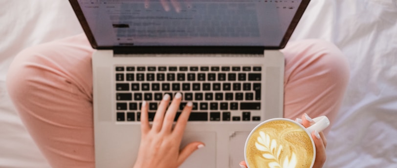 person using MacBook Pro and holding cappuccino