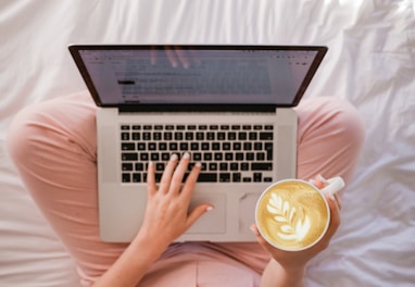 person using MacBook Pro and holding cappuccino