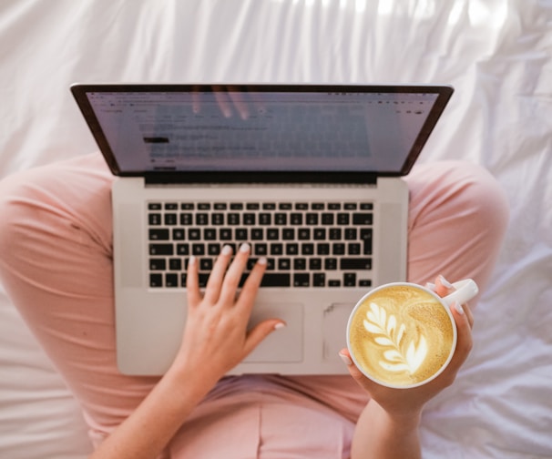 person using MacBook Pro and holding cappuccino