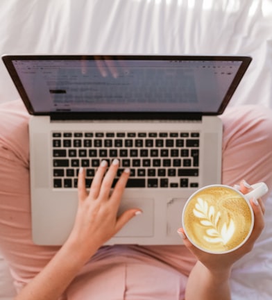 person using MacBook Pro and holding cappuccino