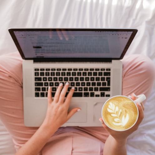 person using MacBook Pro and holding cappuccino