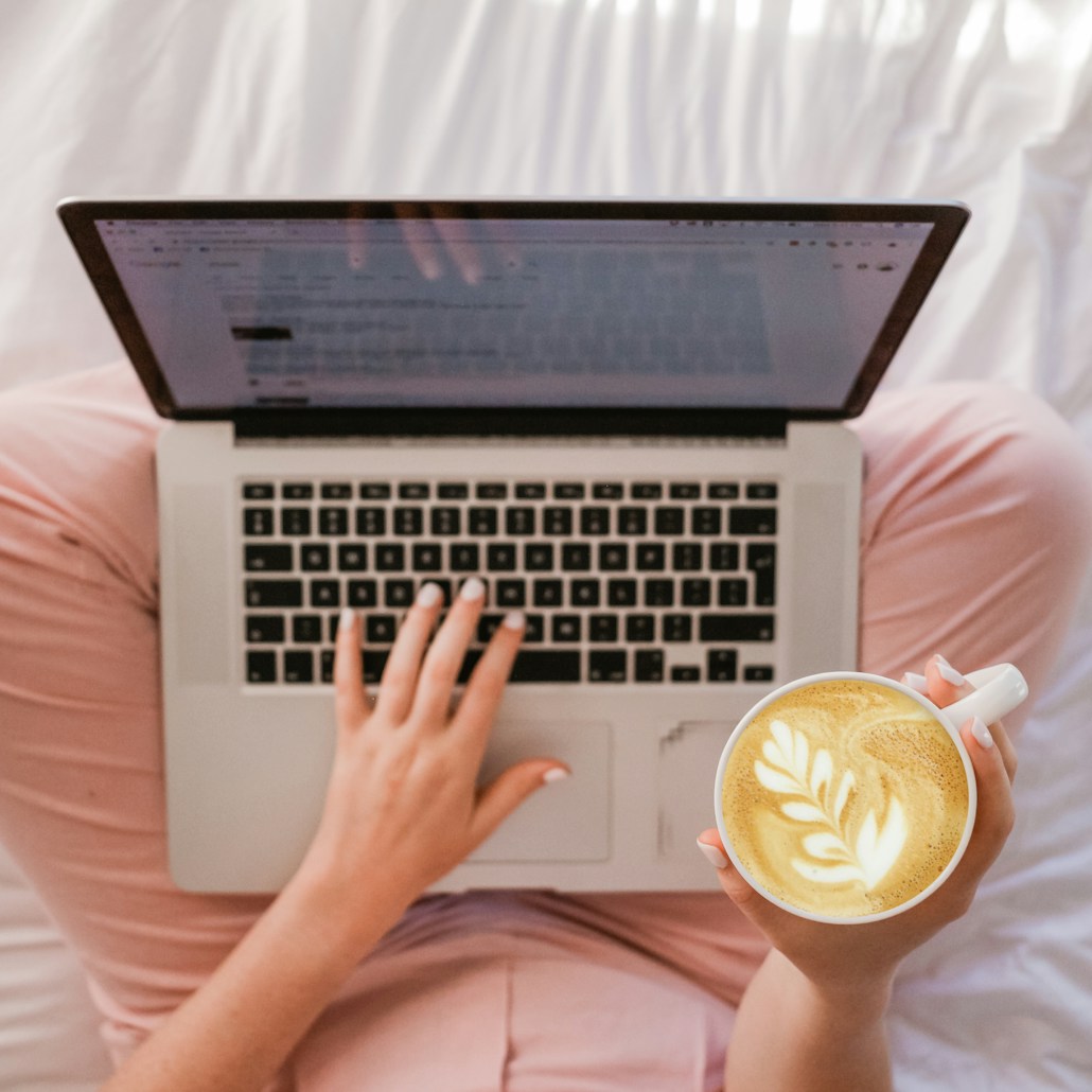 person using MacBook Pro and holding cappuccino