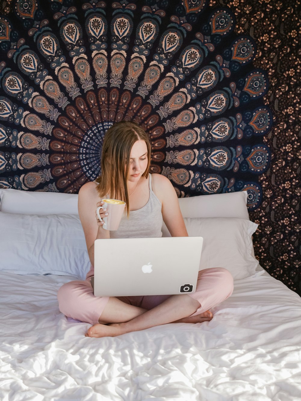 Frau sitzt auf dem Bett mit Laptop und hält Tasse