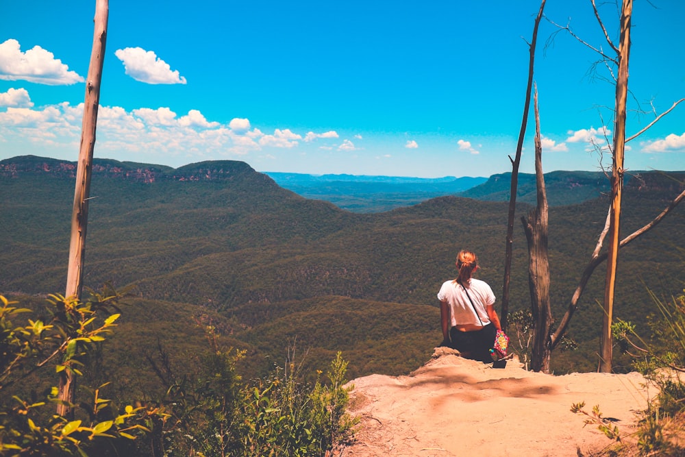 woman sitting on ground watching mountain during daytime