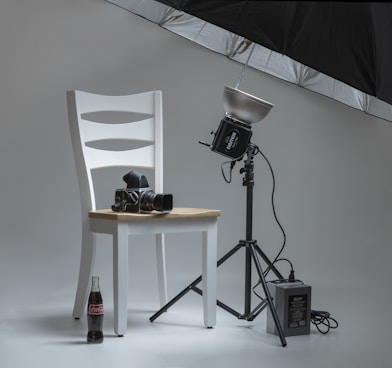 black video camera on white wooden chairs beside photo shooting umbrella