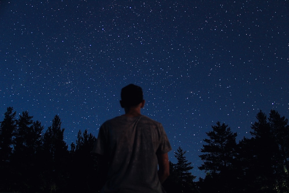 uomo in piedi vicino agli alberi sotto le stelle durante la notte