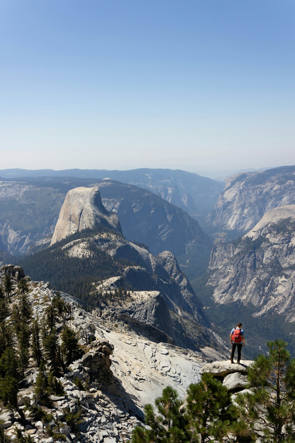 man standing cliff overlooking mountain during daytime