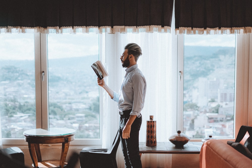 standing man reading book near window