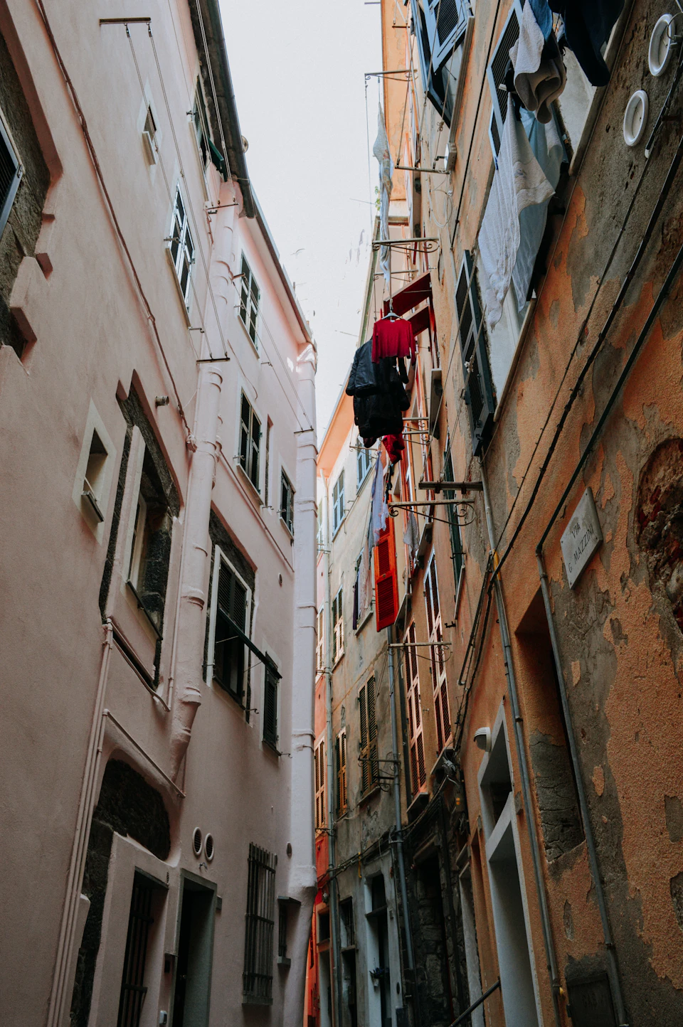 A woman climbs down from a second-floor balcony onto a first-floor balcony in alleyway