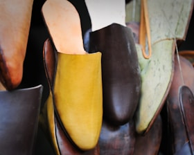 A collection of various colored and styled slippers, prominently featuring a mustard yellow slipper in the center. The slippers are hanging and appear to be made of leather, with some in shades of brown and green.