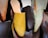 A collection of various colored and styled slippers, prominently featuring a mustard yellow slipper in the center. The slippers are hanging and appear to be made of leather, with some in shades of brown and green.
