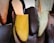 A collection of various colored and styled slippers, prominently featuring a mustard yellow slipper in the center. The slippers are hanging and appear to be made of leather, with some in shades of brown and green.