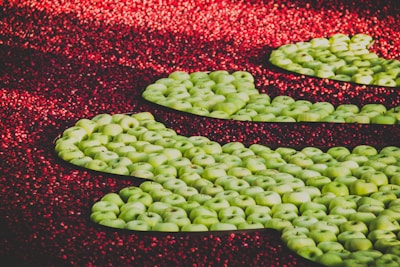 Clusters of green apples are artistically arranged against a backdrop of vibrant red cranberries, creating a striking contrast between the colors.