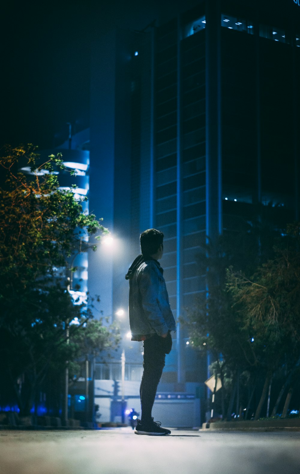 man wearing gray hoodie and black pants standing on street at night