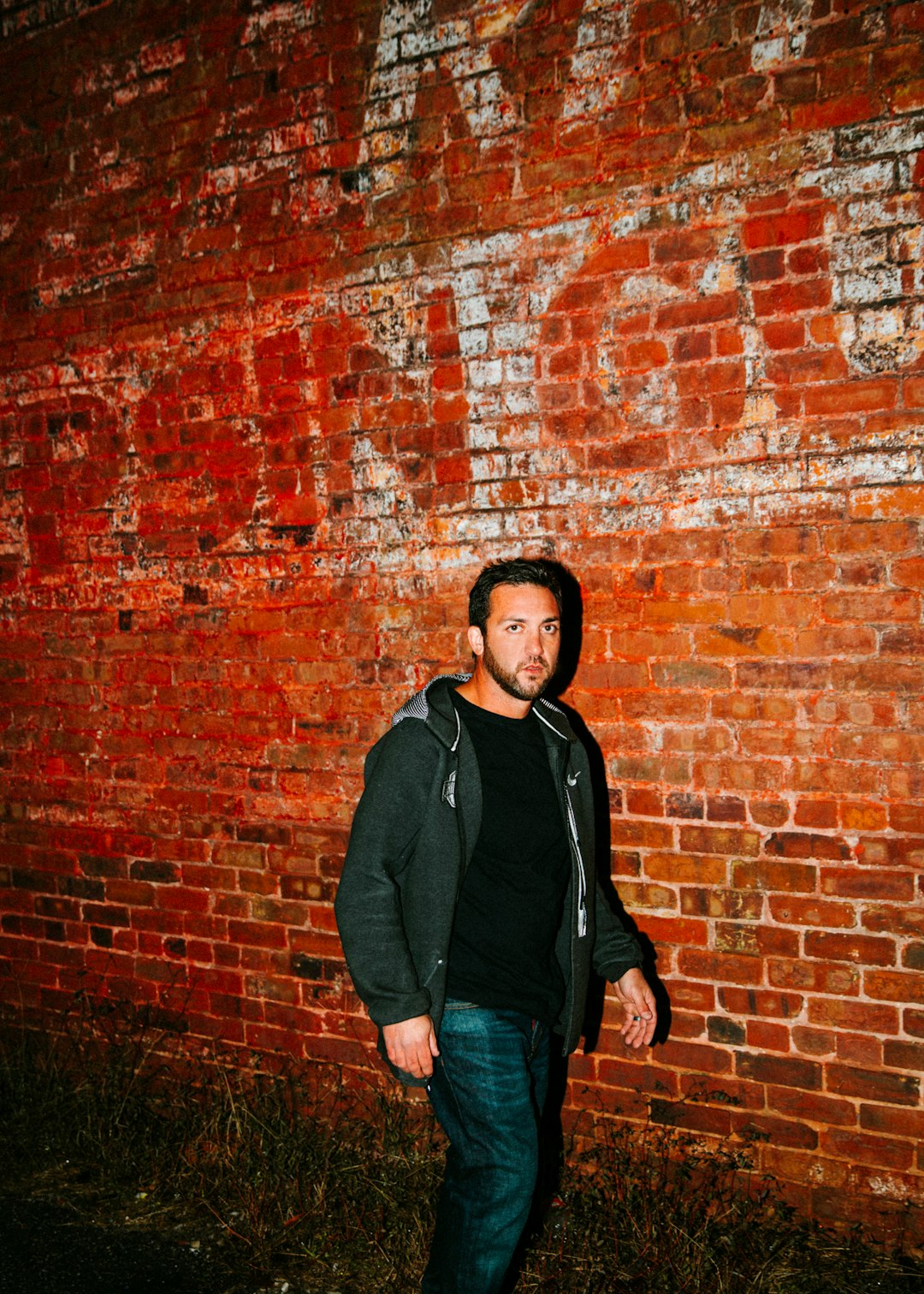 man in black zip-up hoodie walking beside brown bricked wall