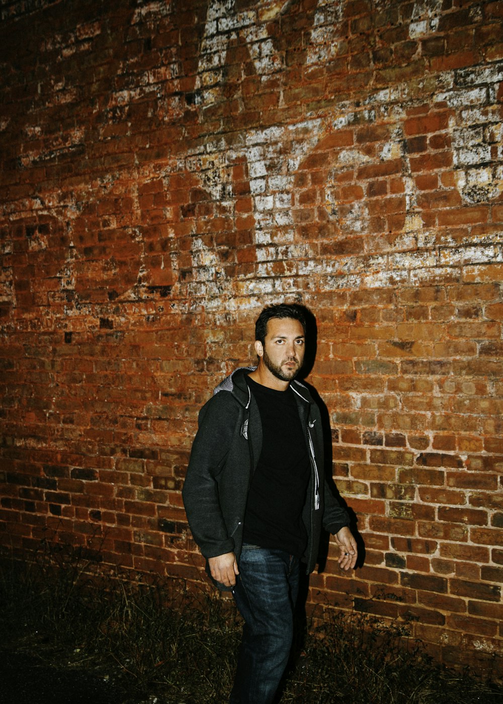 man in black zip-up hoodie walking beside brown bricked wall