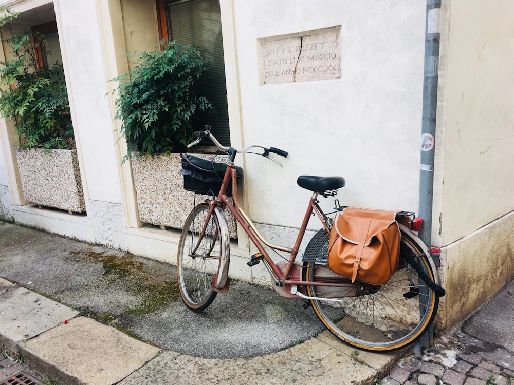 red bike with brown leather saddle bag parked beside white wall during daytime