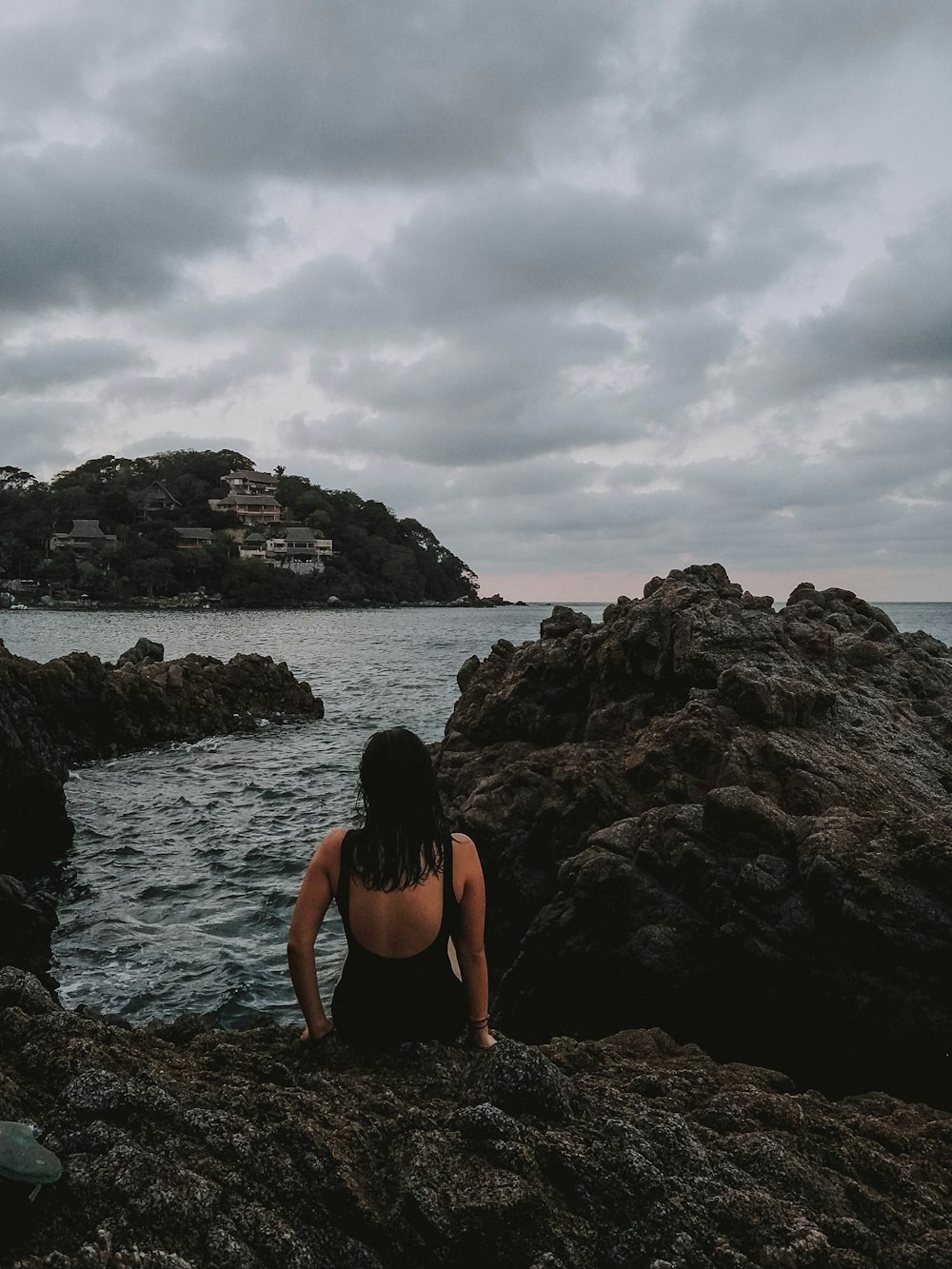 woman wearing black tank monokini sitting on rock formation near body of water during daytime