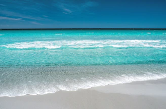 A panoramic view of a serene beach with turquoise waves gently caressing the sand.