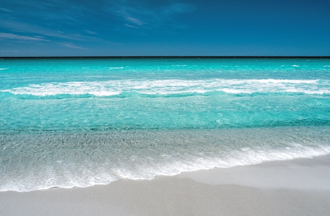 A serene beach scene with turquoise waves gently touching white sandy shore under a clear sky.