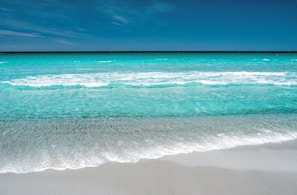 A close-up of turquoise ocean waves gently crashing on a sandy shore under a bright sky