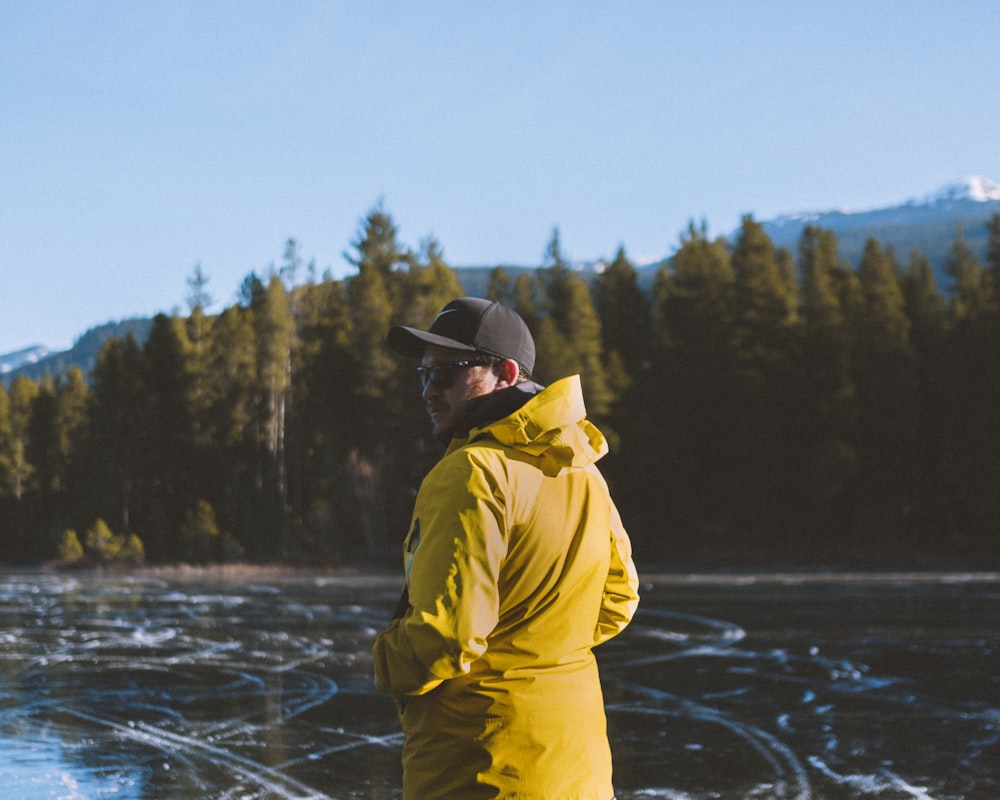 man wearing yellow jacket standing near body of water during daytime