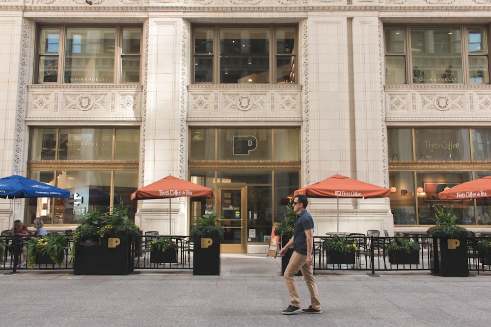 man in black walks past building with red parasols in front