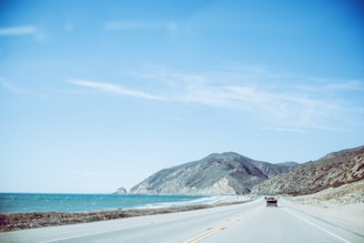 A scenic view of a coastal highway with a car driving along the turquoise sea.