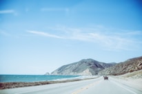 A scenic view of the Pacific Coast Highway winding along the ocean with a tour bus in the distance.