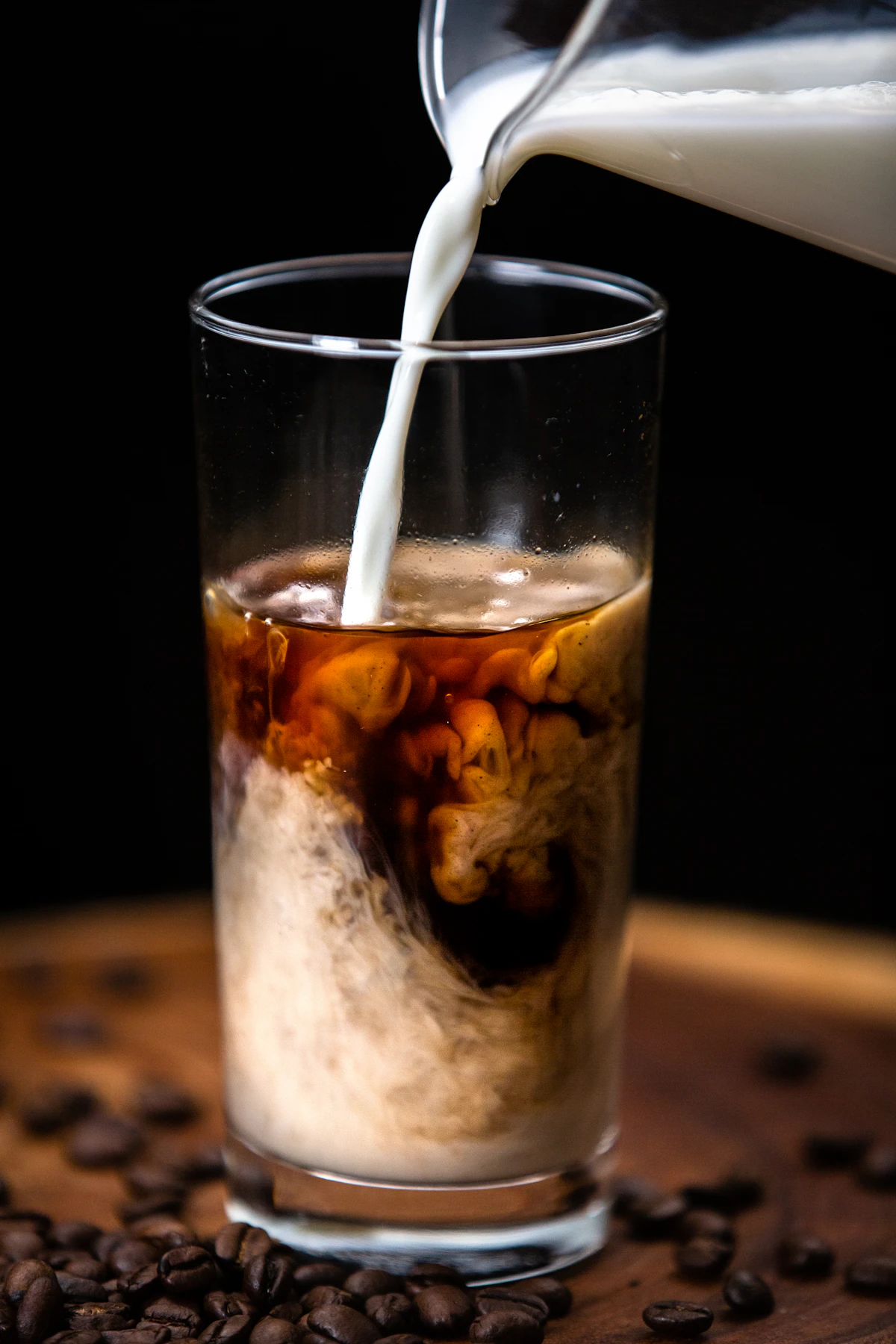 Milk being poured into a glass of dark cold brew coffee, creating a beautiful swirl