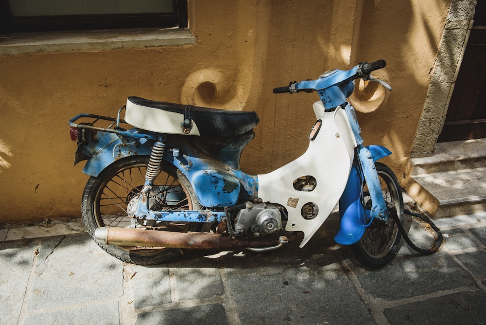 white and blue classic motorcycle parked beside brown wall