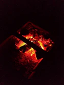 Close-up of glowing embers in a charcoal fire pit, casting a warm amber light.