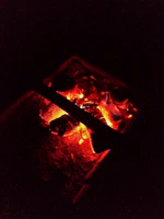 Close-up of glowing embers in a rustic fire pit, casting warm light.