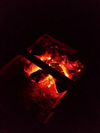 Close-up of glowing embers in a charcoal fire pit, casting a warm amber light.
