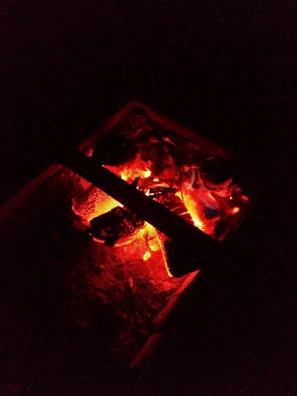 Close-up of glowing embers in a rustic fire pit, casting warm light.