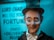 A vintage fortune-teller automaton with a smiling expression, wide-open blue eyes, and rosy cheeks. It wears a black top hat, a black suit, and a white shirt beneath. Behind it, a blurred sign reads 'Lord Charles will tell your fortune,' creating a mystical atmosphere with blue lighting.