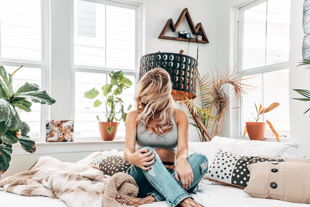 woman in gray sports bra sitting on bed near windows