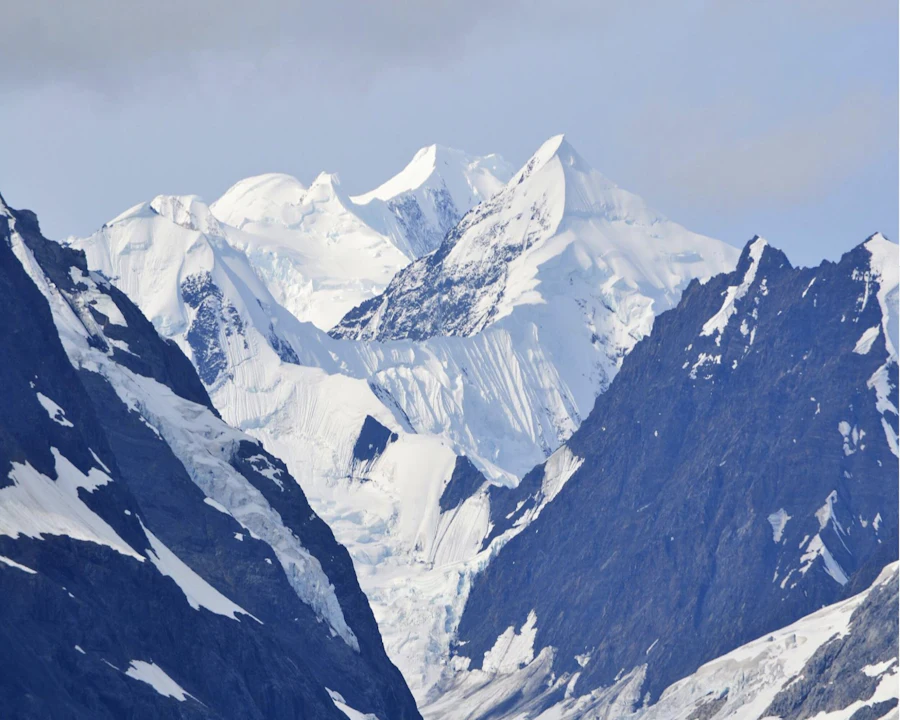 Aerial view over a folded range of green and snow-streaked mountains