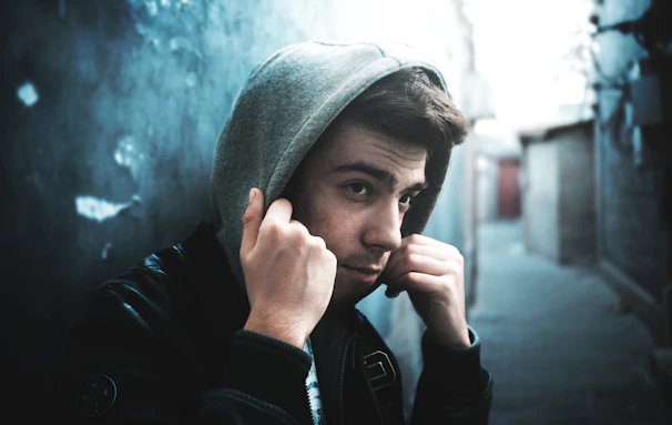 A candid shot of a person adjusting the hood of a plain oversized hoodie outdoors in soft daylight.