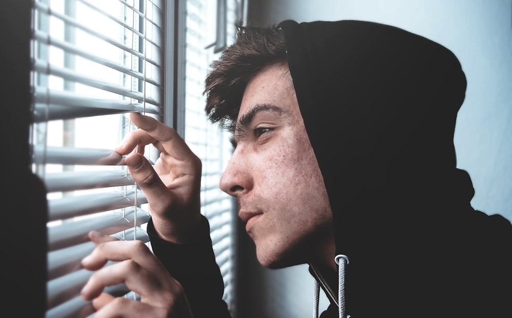 man holding white window blinds while looking outside